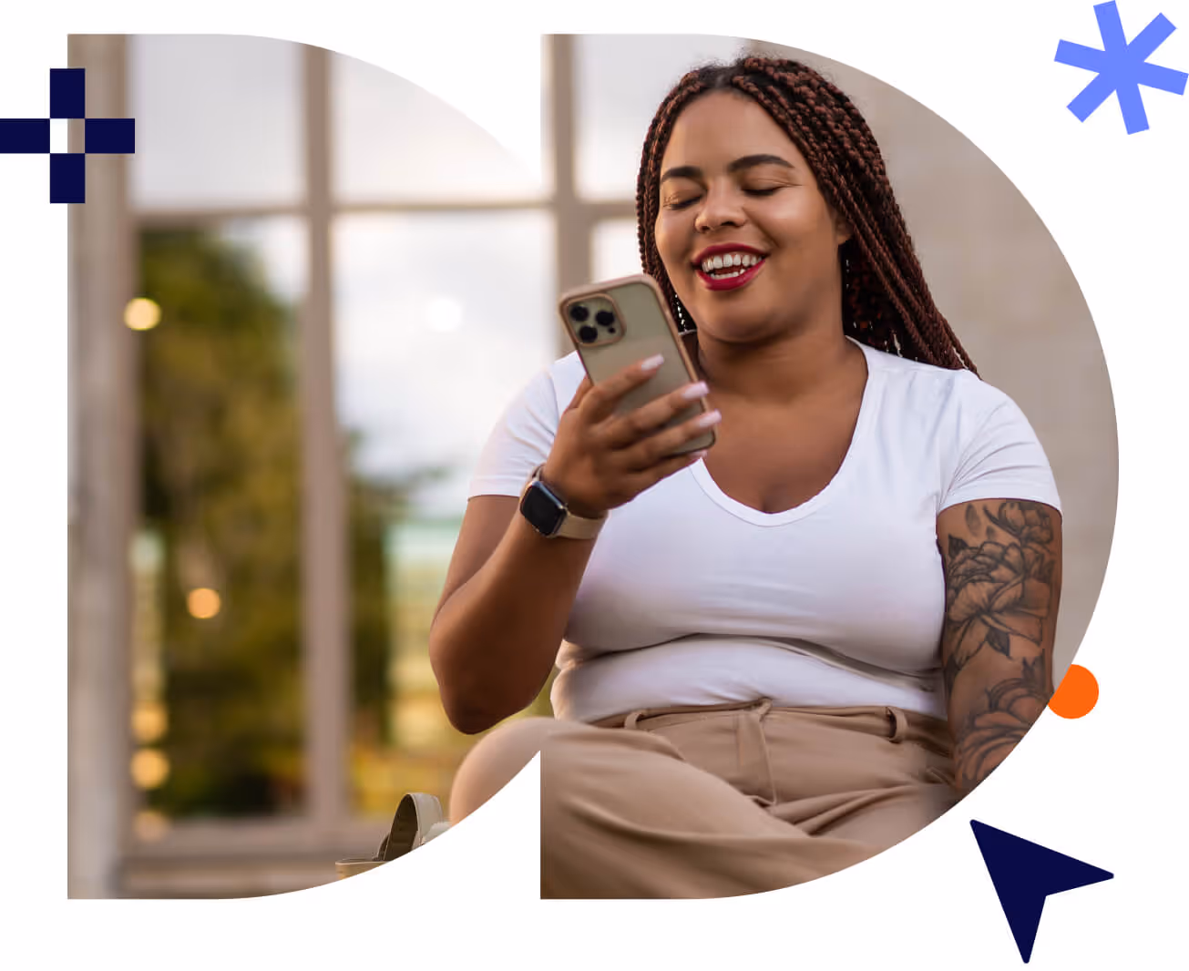 Smiling woman with braided hair looking at her smartphone while sitting indoors near a window.