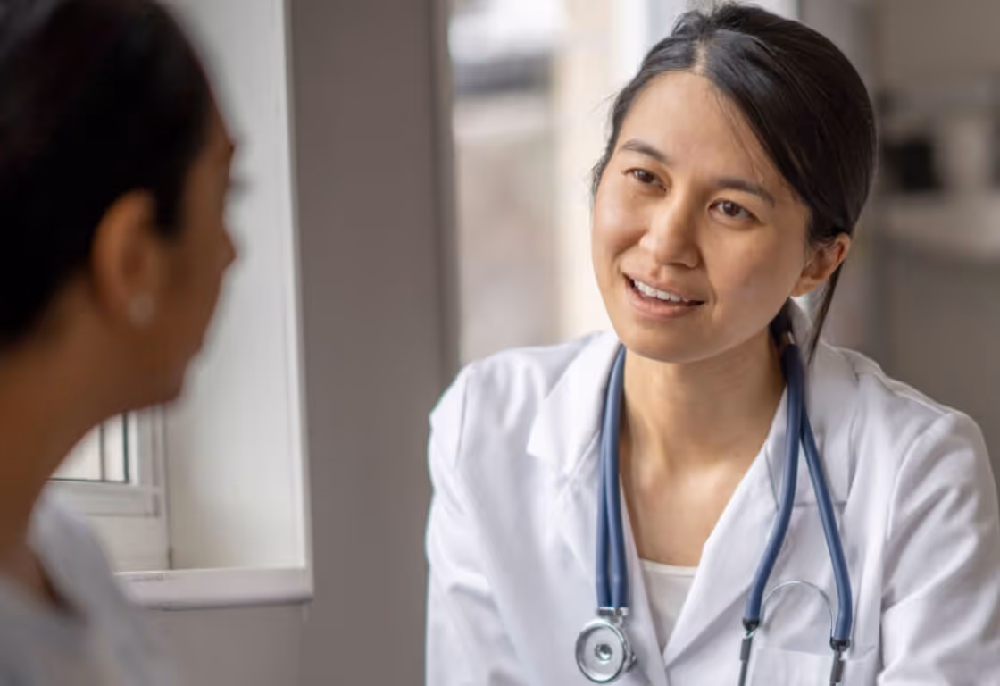 Female doctor with stethoscope speaking to a patient in a consultation room.