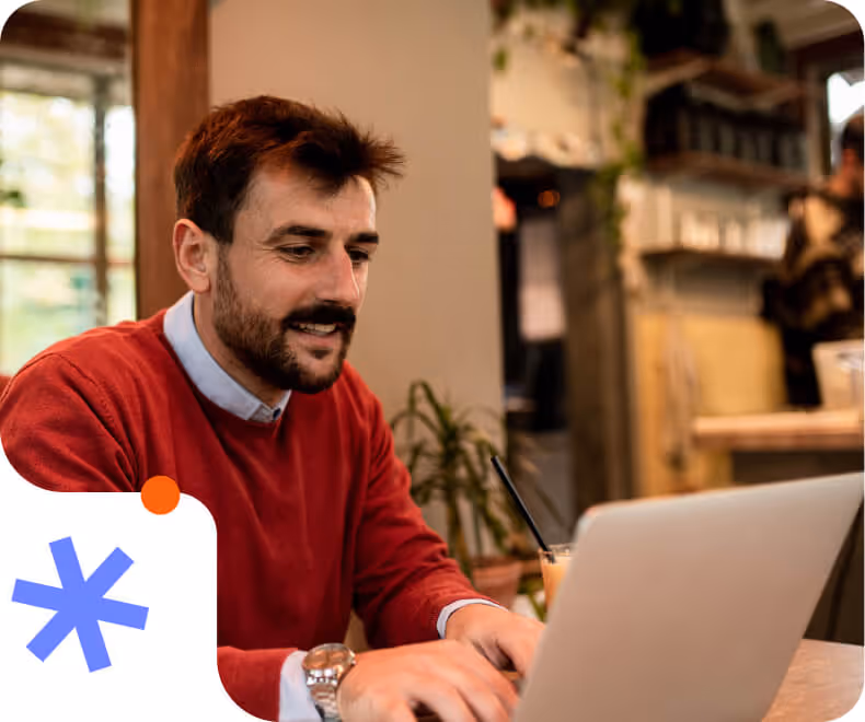 Man in a red sweater working on a laptop at a cozy indoor café.