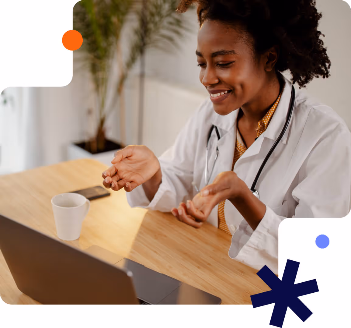 Smiling female doctor in a white coat with stethoscope conducting a video consultation on a laptop.