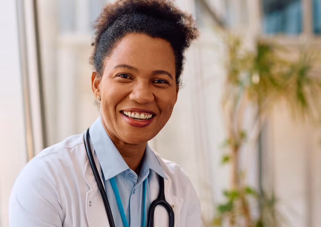 Smiling female doctor wearing a white coat and stethoscope in a bright medical office.