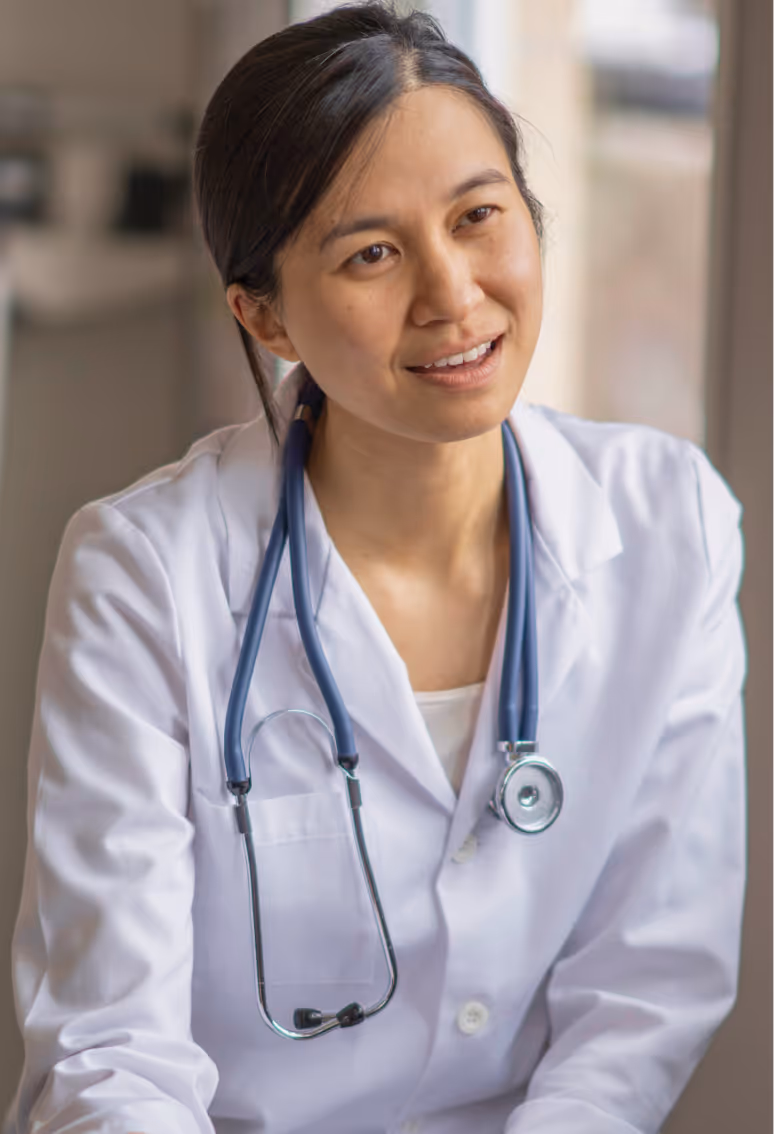 Female doctor wearing white coat with a stethoscope around her neck, looking engaged and smiling.