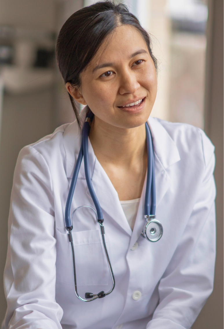 Female doctor wearing white coat with a stethoscope around her neck, looking engaged and smiling.