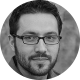 Portrait of a man with glasses, facial hair, and short dark hair, looking at the camera.