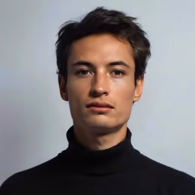 Young man with short dark hair wearing a black turtleneck against a plain background.
