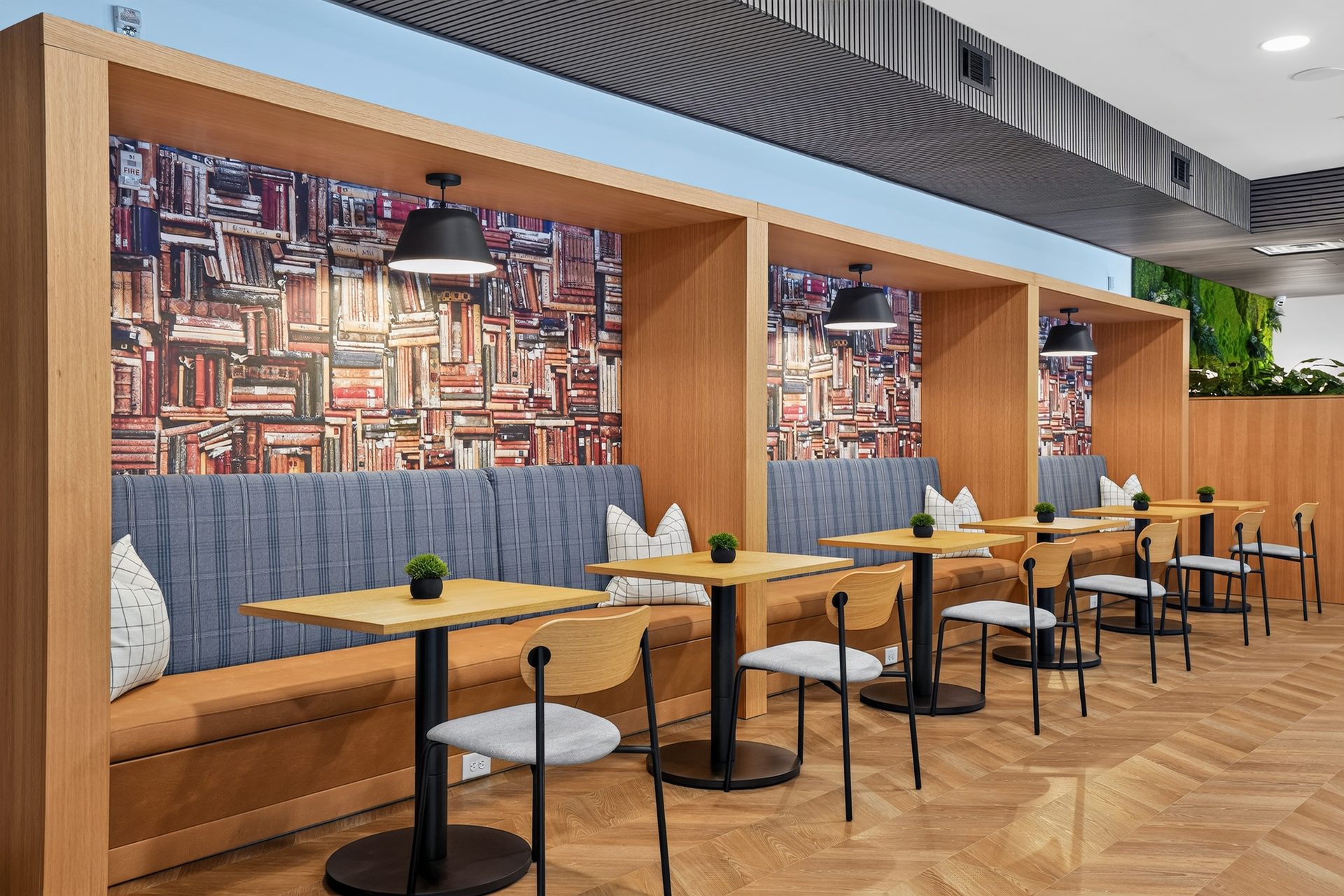 Wood-framed study booths with bookshelf wallpaper, pendant lights, and two-person tables