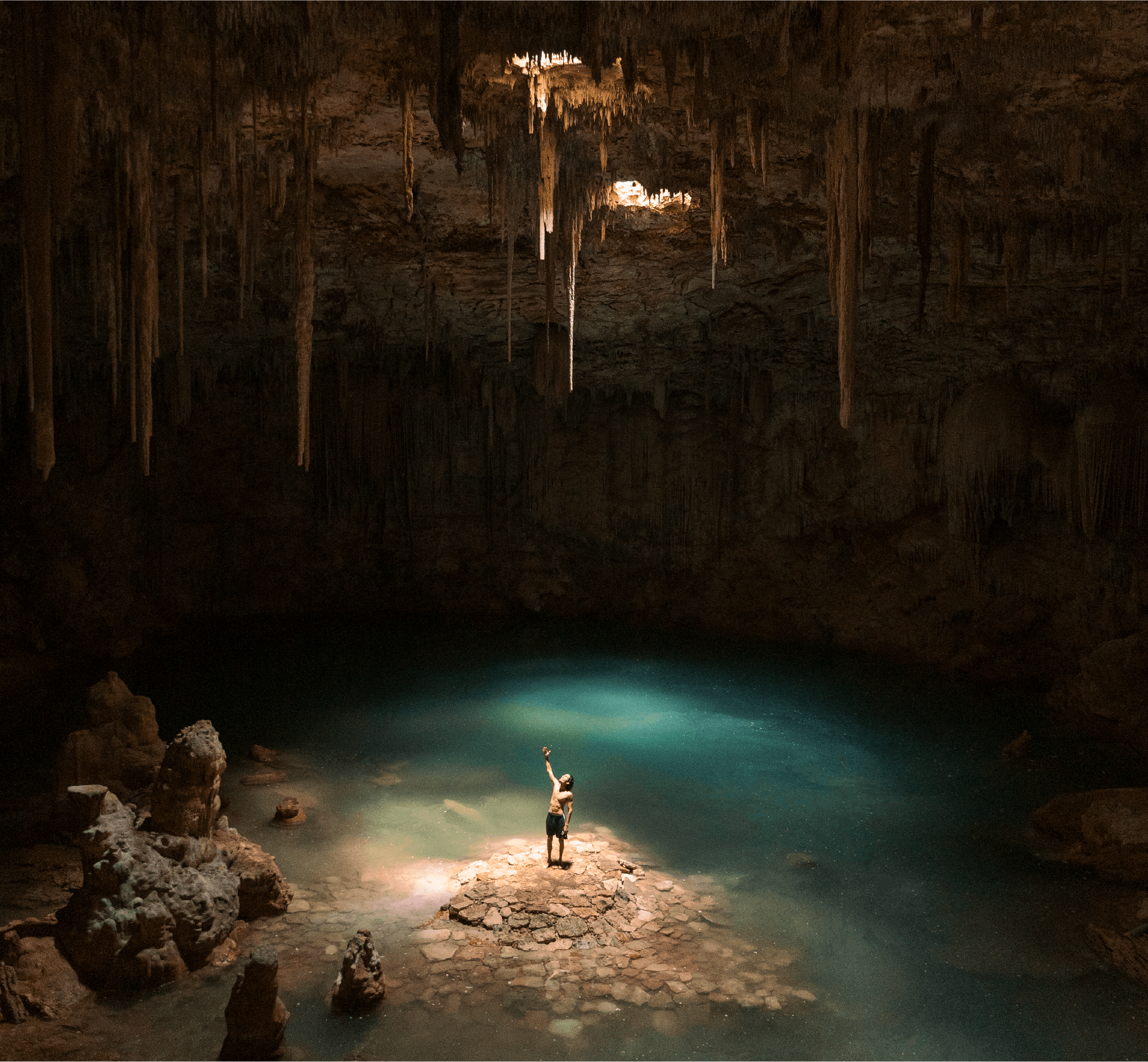 Persona de pie sobre una roca en el centro de un cenote iluminado