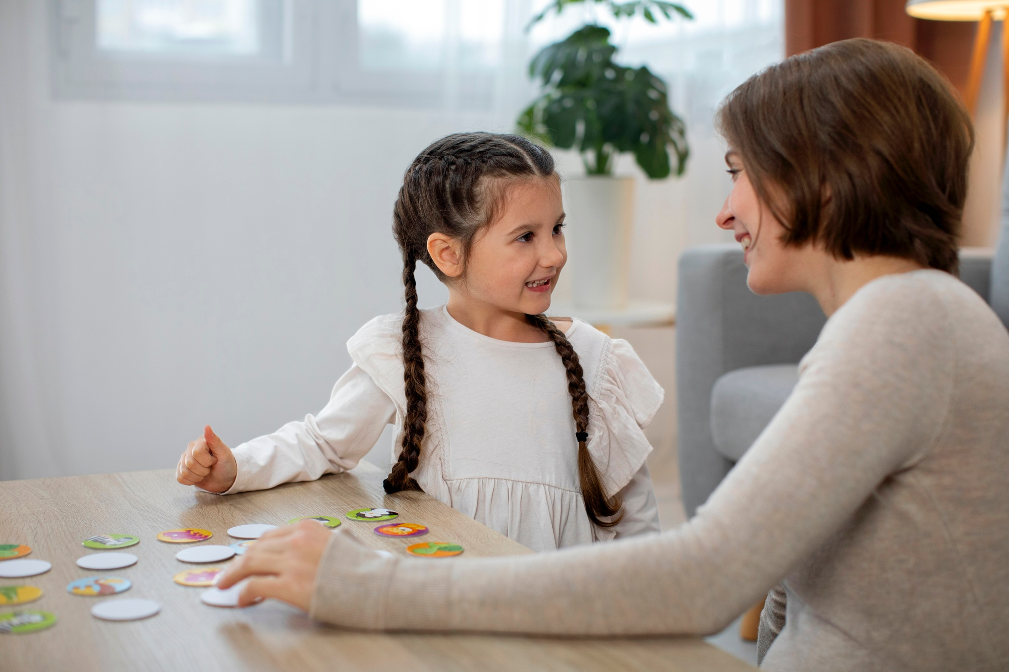 Mother and young daughter smiling and playing a matching card game at a wooden table indoors.