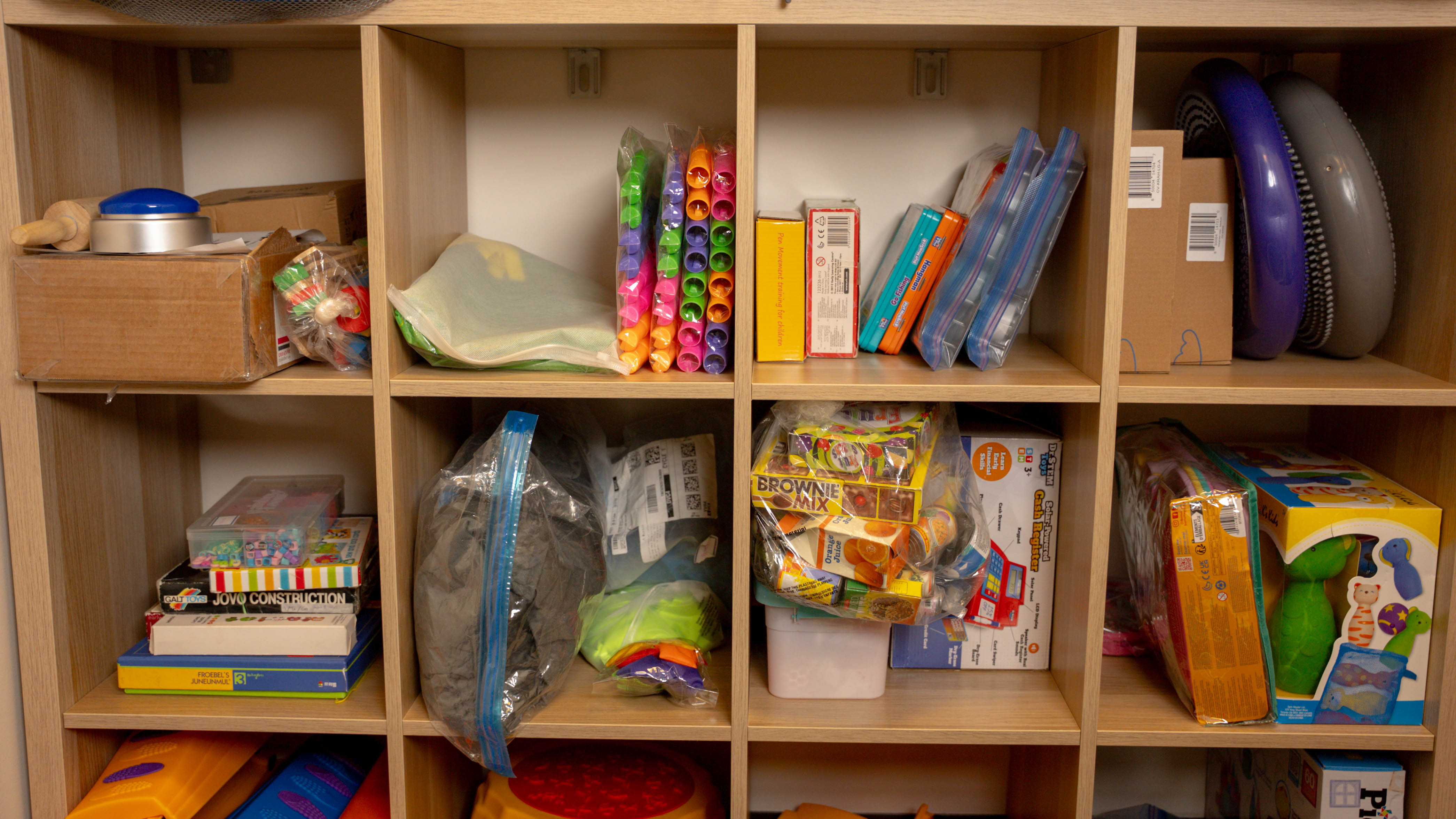 Wooden cubby shelves filled with educational toys, games, and supplies in plastic bags and boxes.