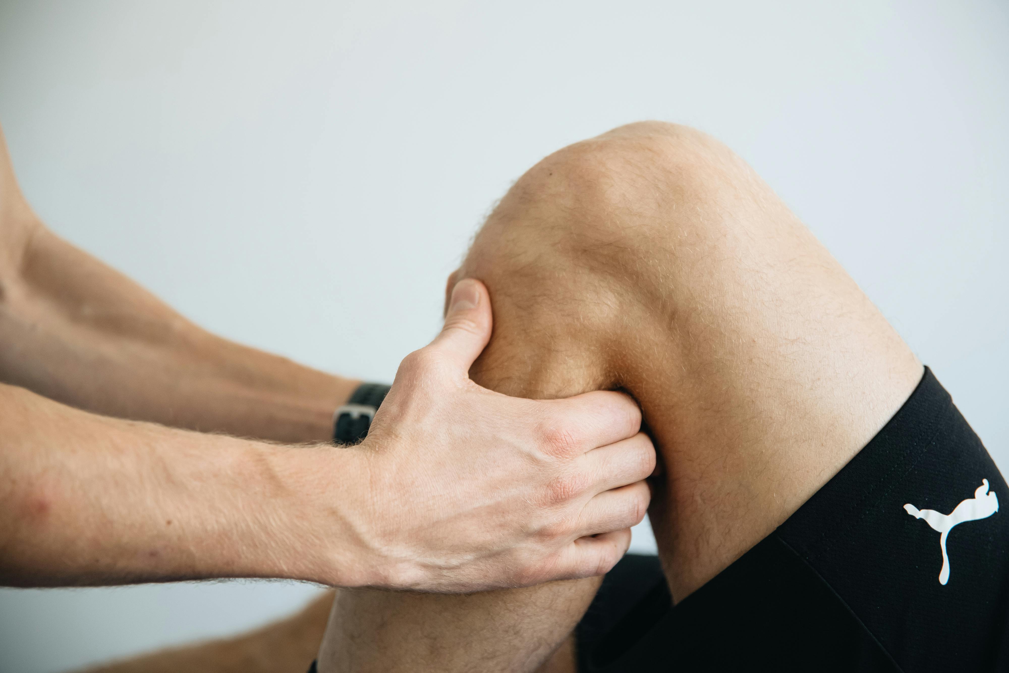 A person holding and massaging their bent knee while wearing black Puma shorts.