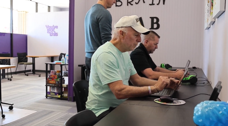 Three men using laptops at a long black table in a bright, modern room labeled Brain Lab.