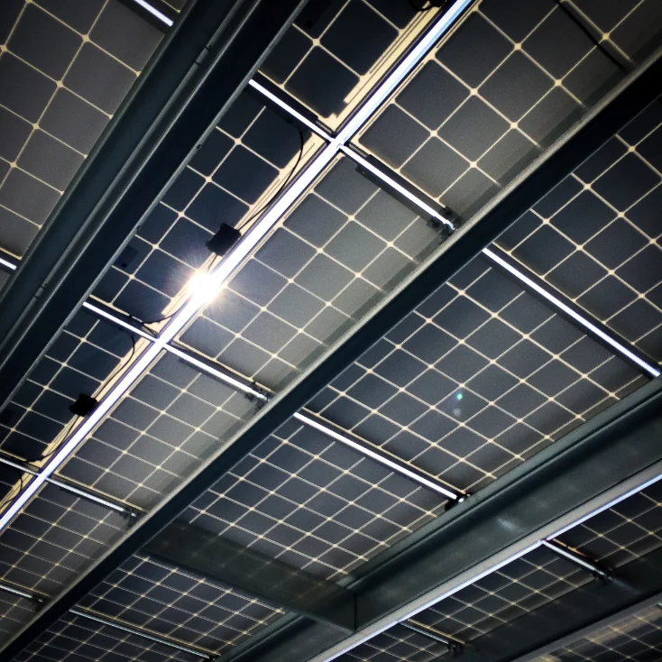 Paneles solares vistos desde abajo con el sol brillando a través de ellos.