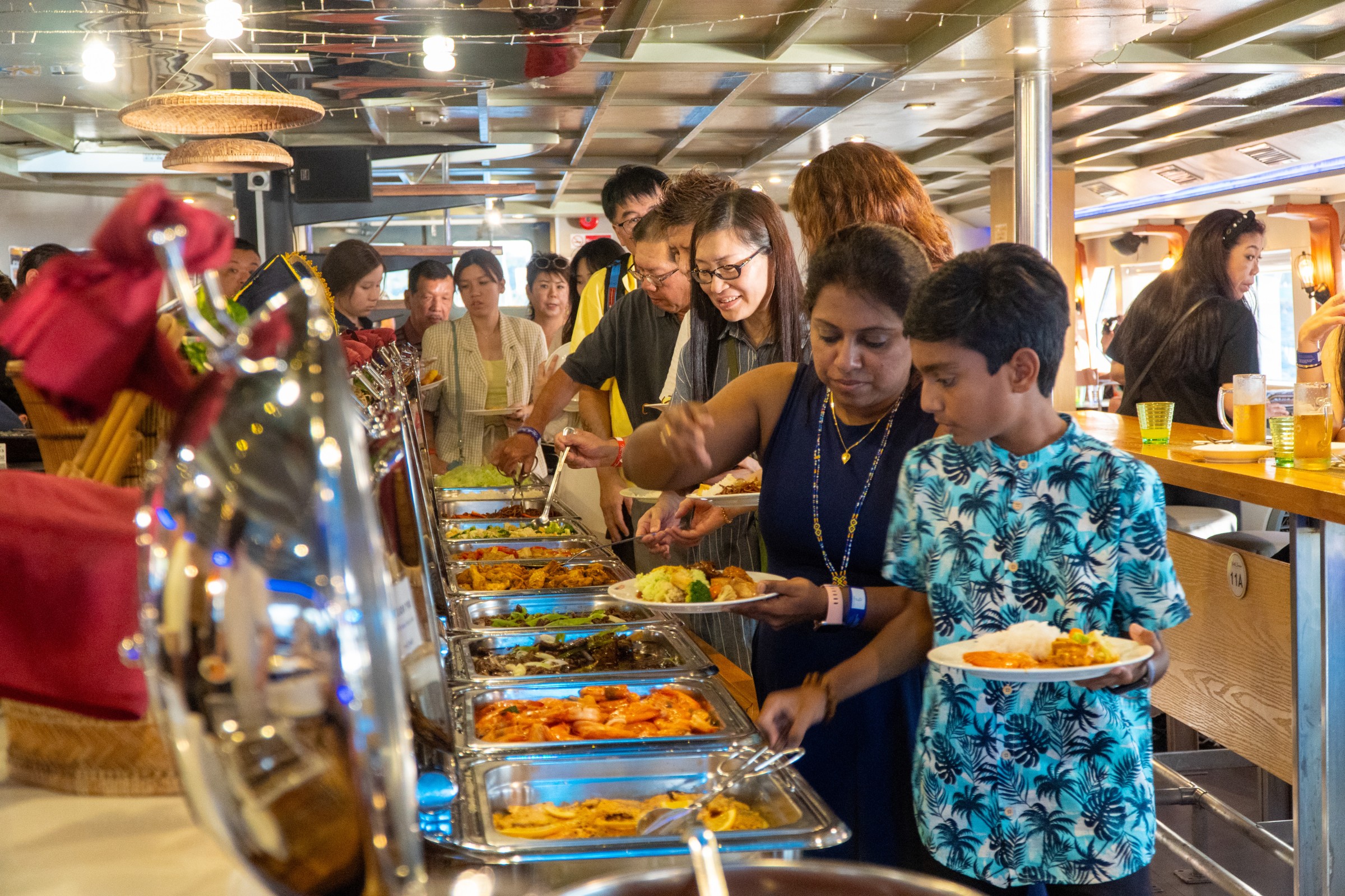 International guests serving themselves food from a buffet line inside North Borneo Cruise.
