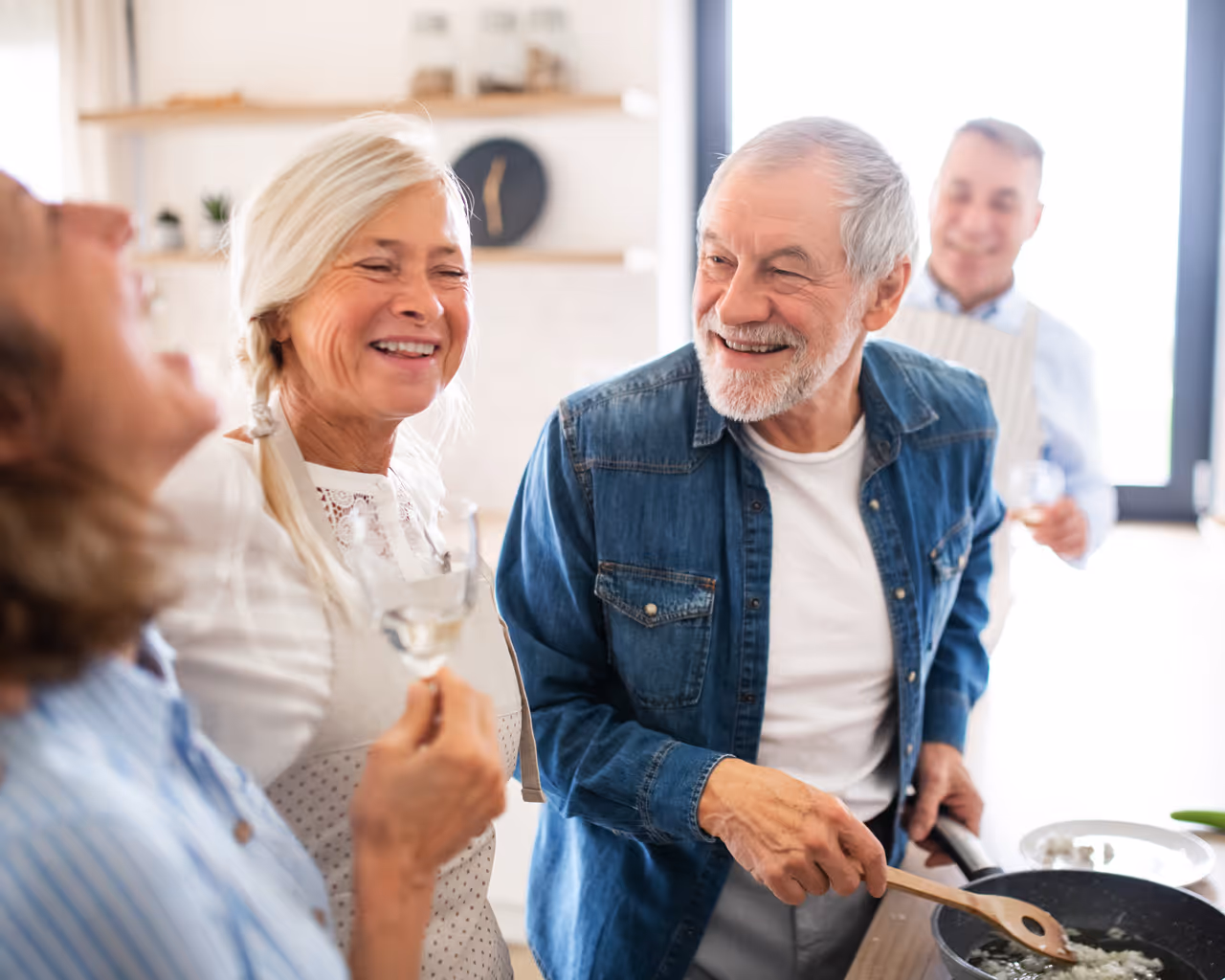 Front view of group of cheerful senior friends at dinner party at home, cooking.