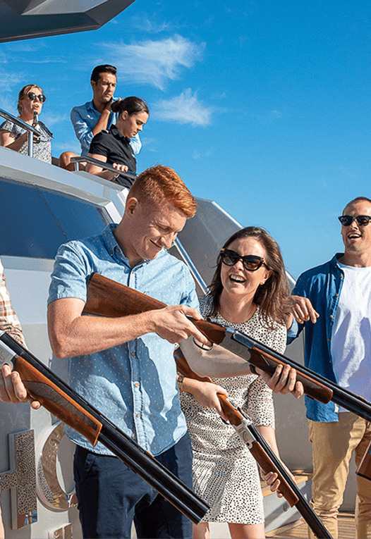 Group of young adults smiling and handling shotguns outdoors on a sunny day.