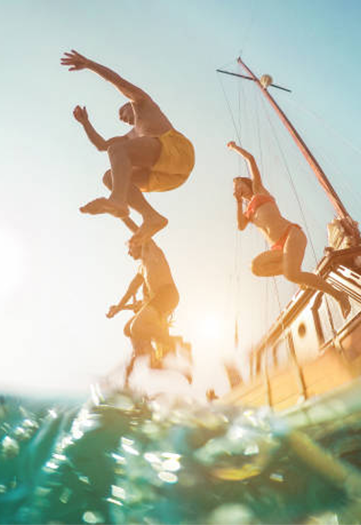 Four people jumping off a boat into the water on a sunny day.