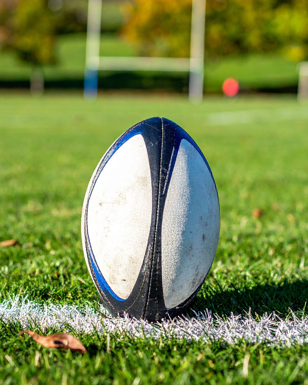 Rugby player in light blue jersey holding ball and evading two opponents in maroon jerseys during a match.