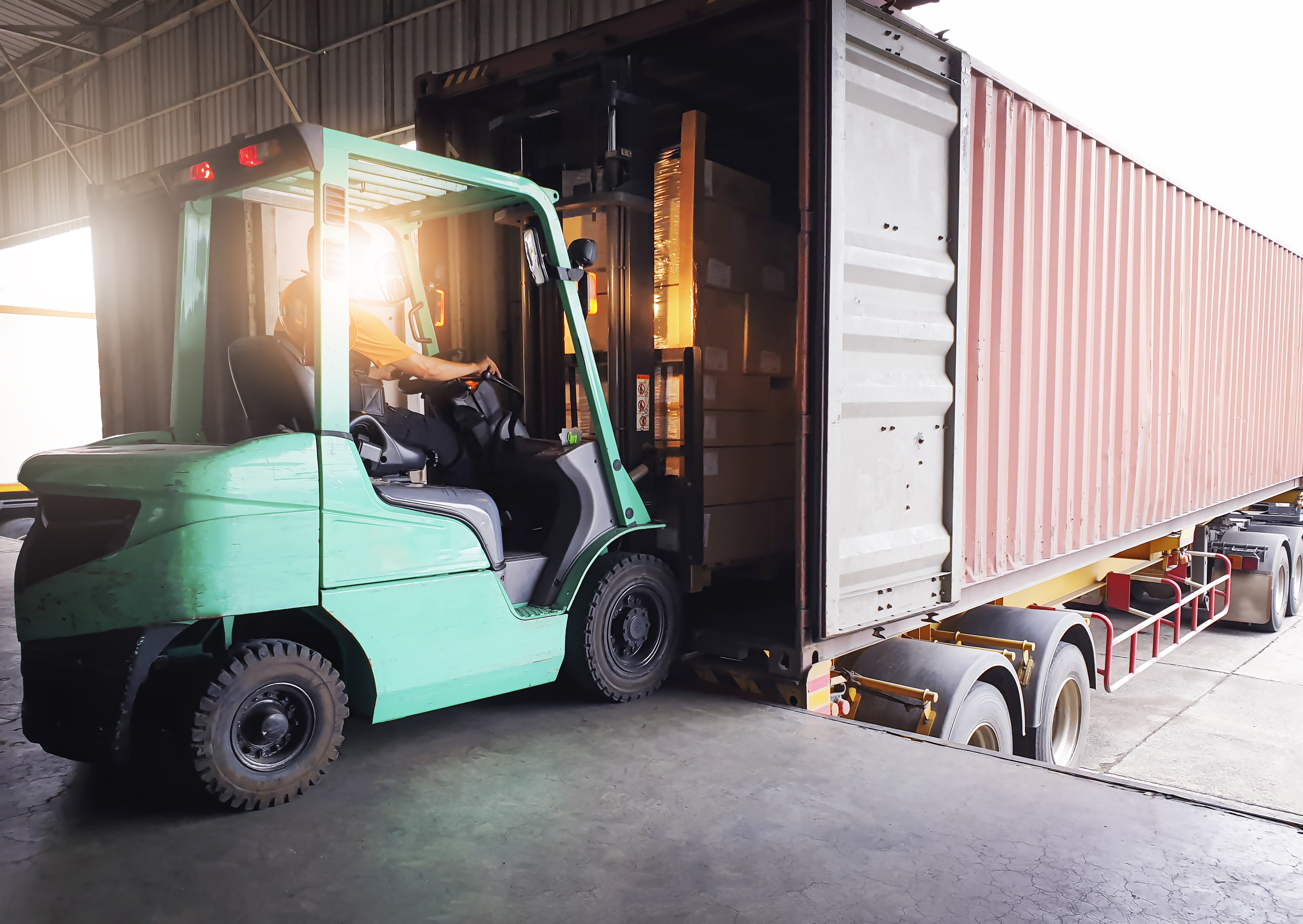 Forklift loading cargo into shipping container at warehouse