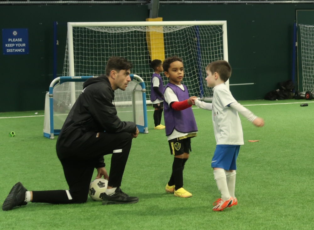 Coach talking to two children who are fist bumping before they begin playing their 1v1 match