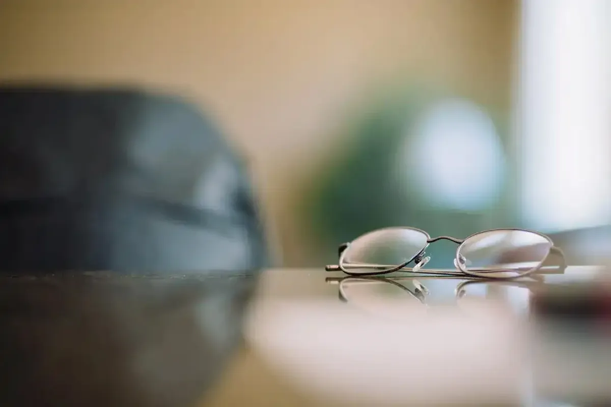 A pair of eyeglasses resting on a reflective surface with a blurred background.