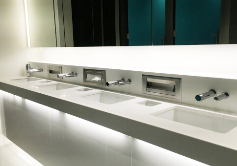 Modern commercial restroom sinks with sleek faucets and built-in hand dryers on a white countertop.