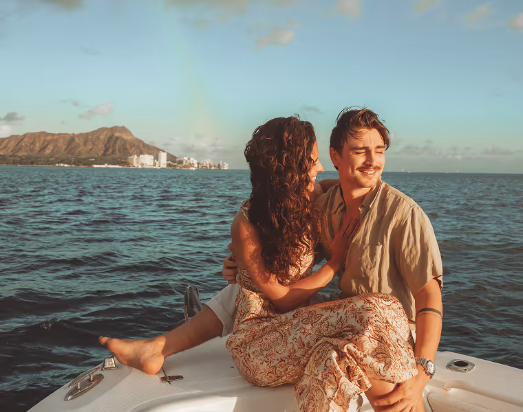 A couple sitting at the bow of the Hawaii Apex Charters boat on a sunset boat tour with the Waikiki skyline and Diamond Head in the background.
