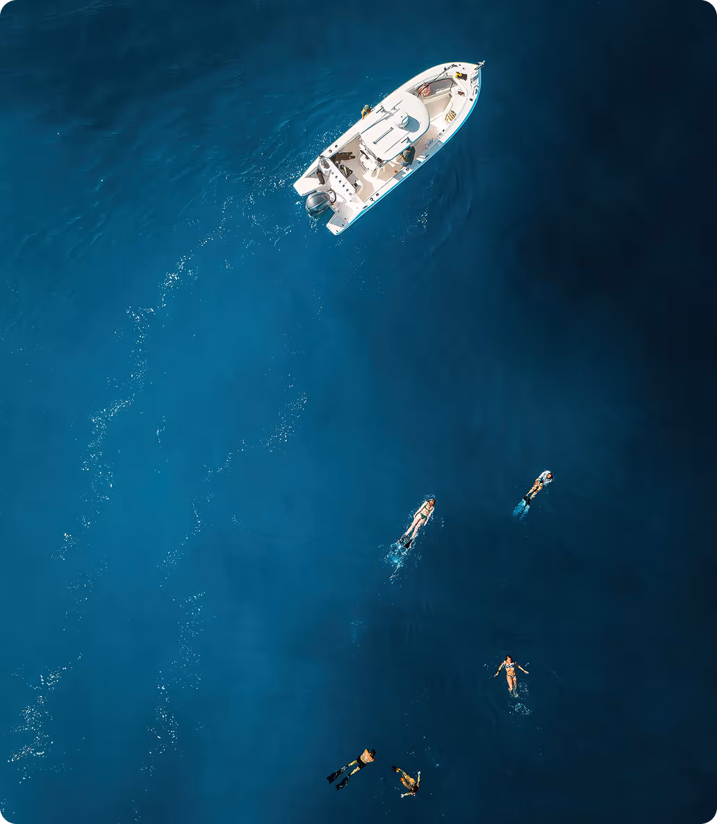 Direct overhead shot of Hawaii Apex Charters small group charter vessel, with a group of snorkelers swimming in blue ocean. 