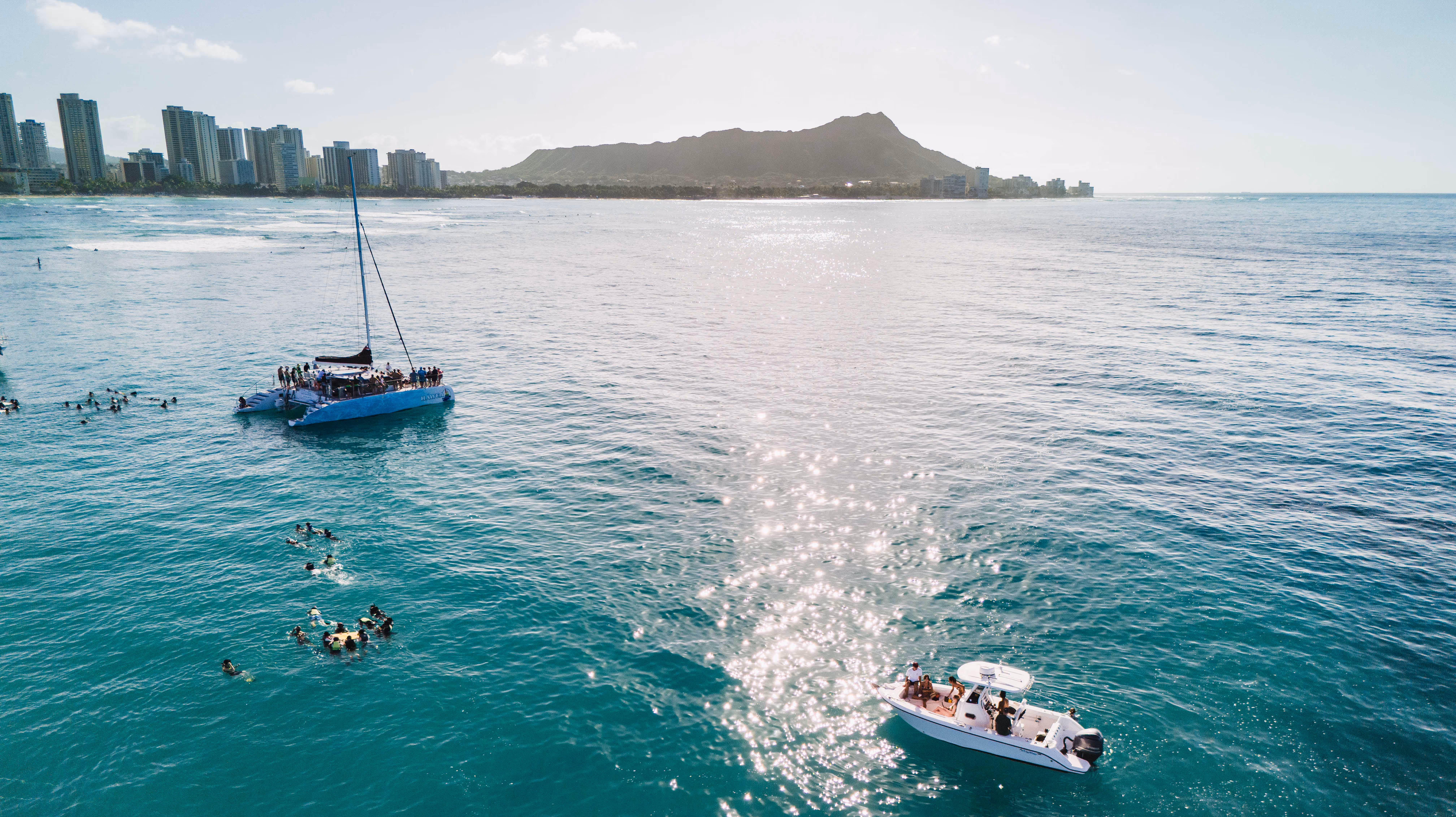 A drone shot of our six pac boat, with the Waikiki coastline and Diamond head outlined in the background.