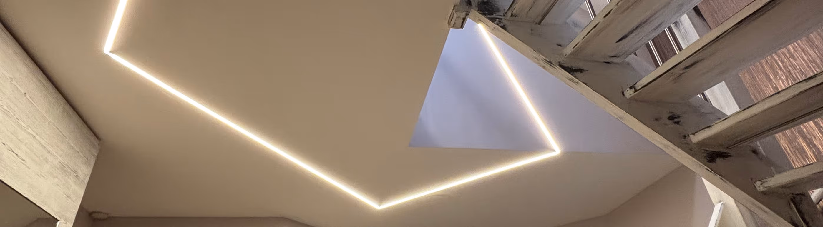 Decke mit eingebauten LED-Lichtstreifen und einer offenen Treppe aus Holz mit natürlichem Licht von oben.