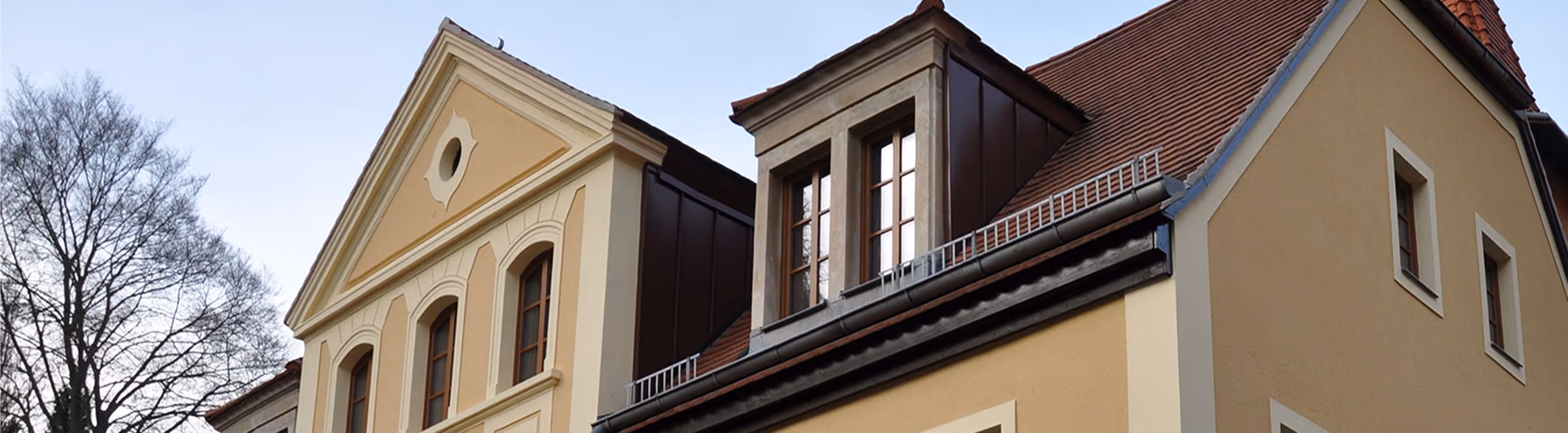 Ansicht eines gelben Gebäudes mit roten Ziegeldächern und mehreren Fenstern bei klarem Himmel.