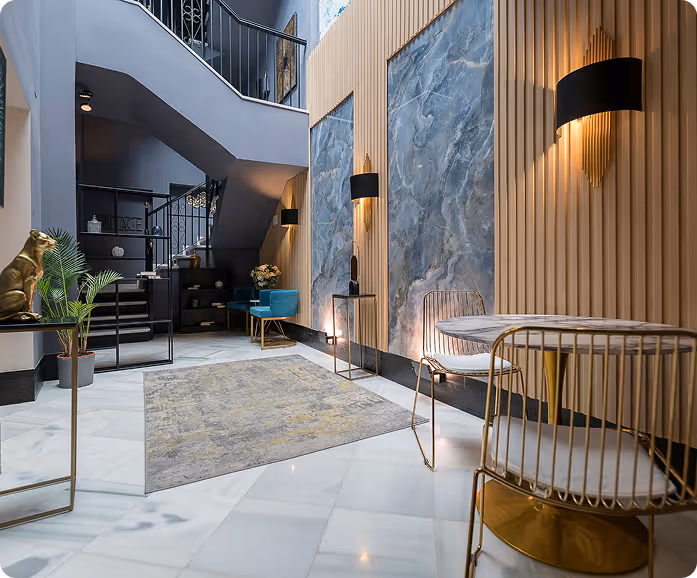Modern interior with white marble floor, gray staircase, blue velvet chairs, decorative gold accents, and large stone wall panels.
