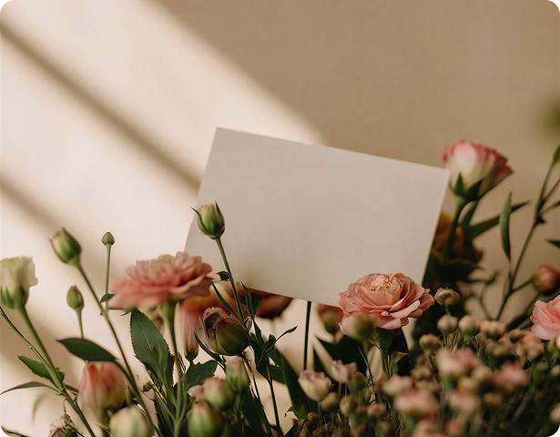 A bouquet of pink and white flowers with a blank white card in the center against a soft beige background.