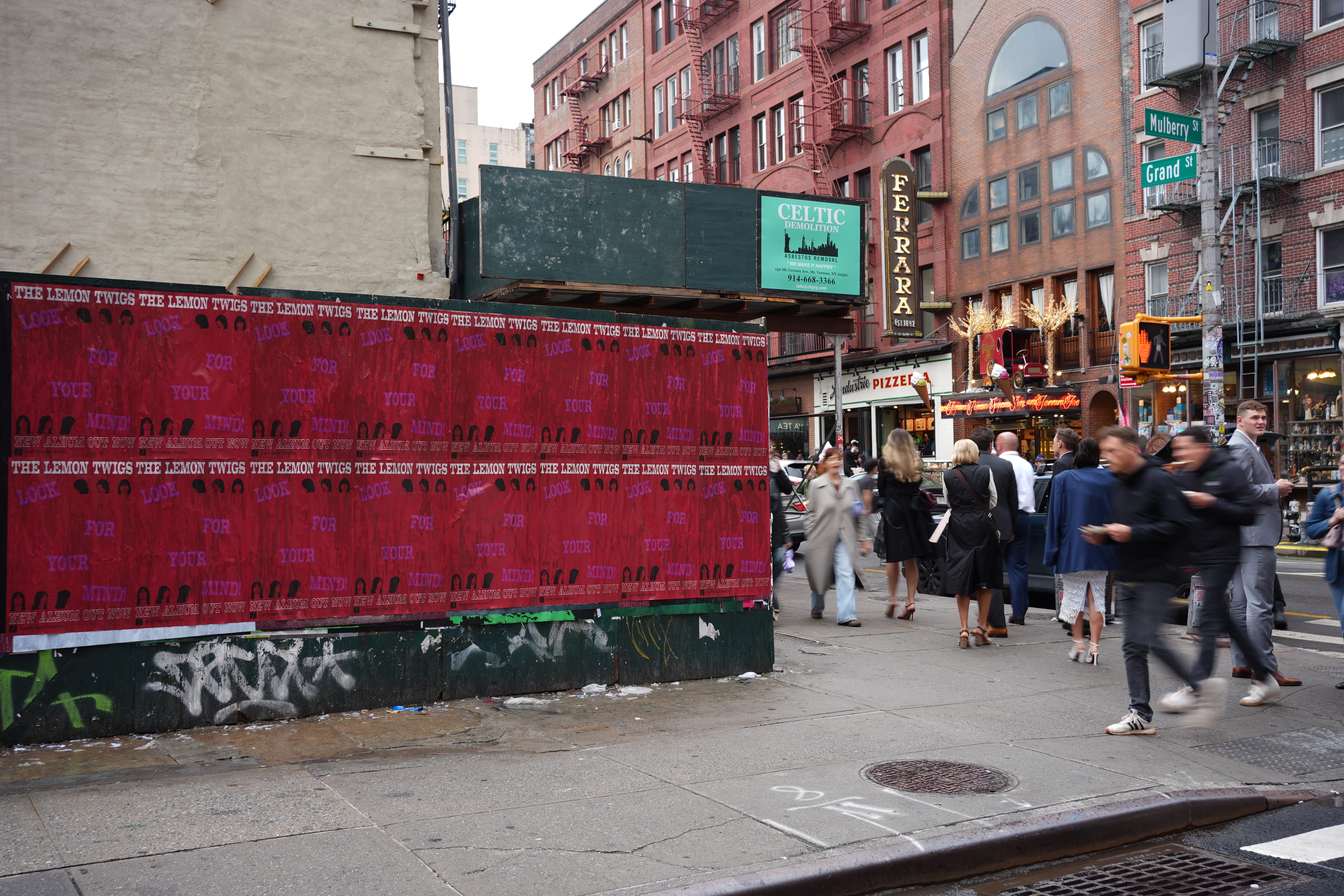 City street with a row of posters advertising the album '$10 Cowboy' featuring a man kicking with a blue horse silhouette.