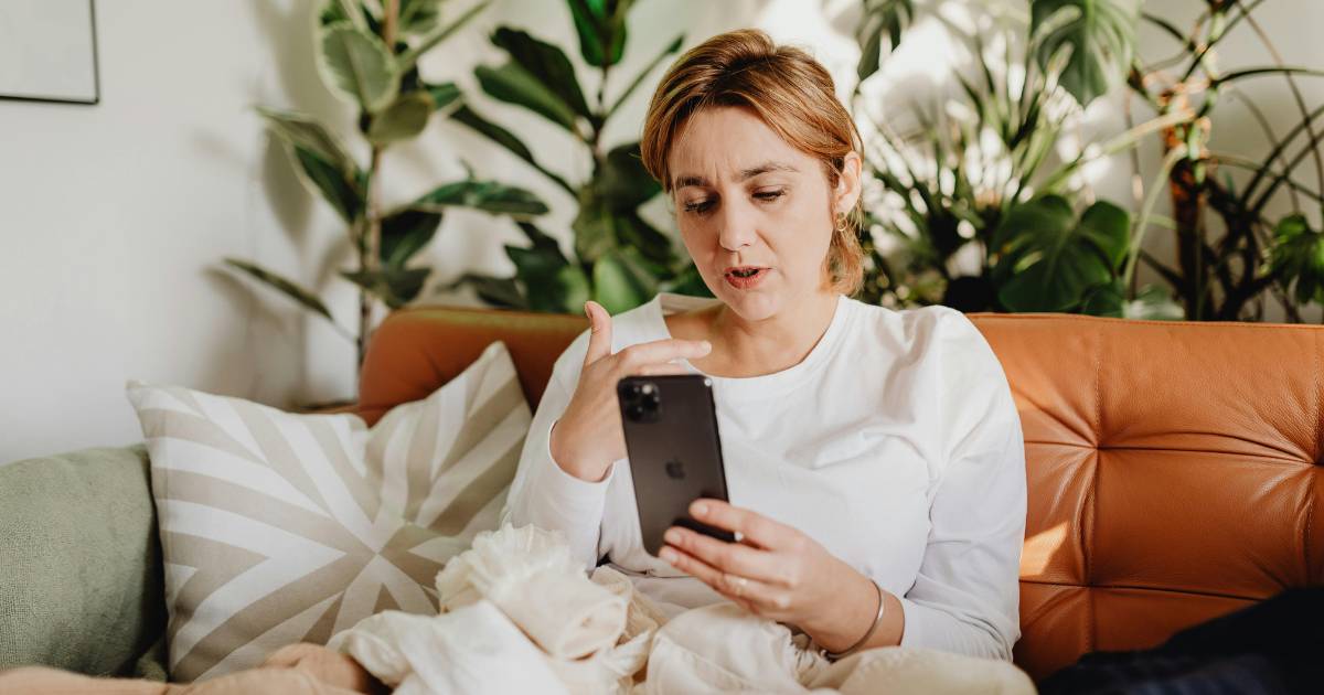 Woman talking into smartphone at home, on the sofa.