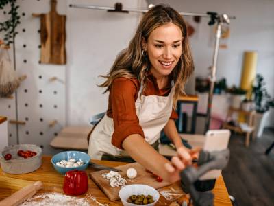 Female food blogger preparing pizza and recording video on smart phone.