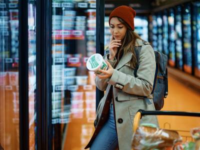 Young woman buying dairy product and reading food label in grocery store.