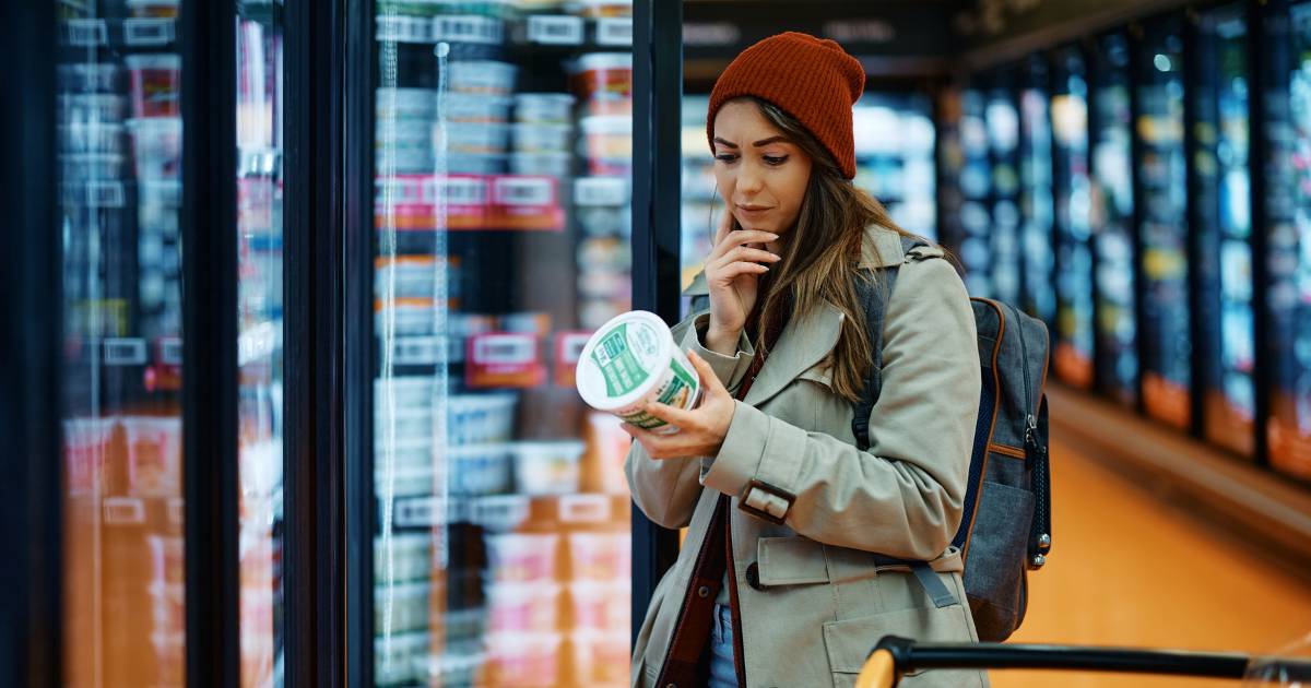 Young woman buying dairy product and reading food label in grocery store.