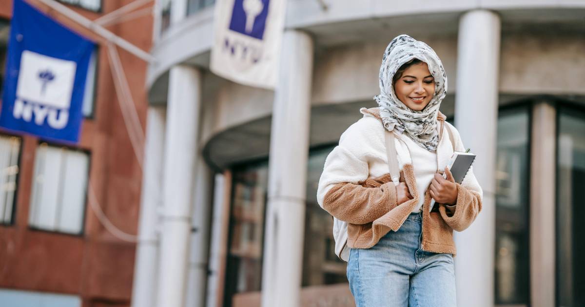 Delighted young ethnic female millennial standing near university building after studies