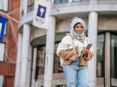 Delighted young ethnic female millennial standing near university building after studies
