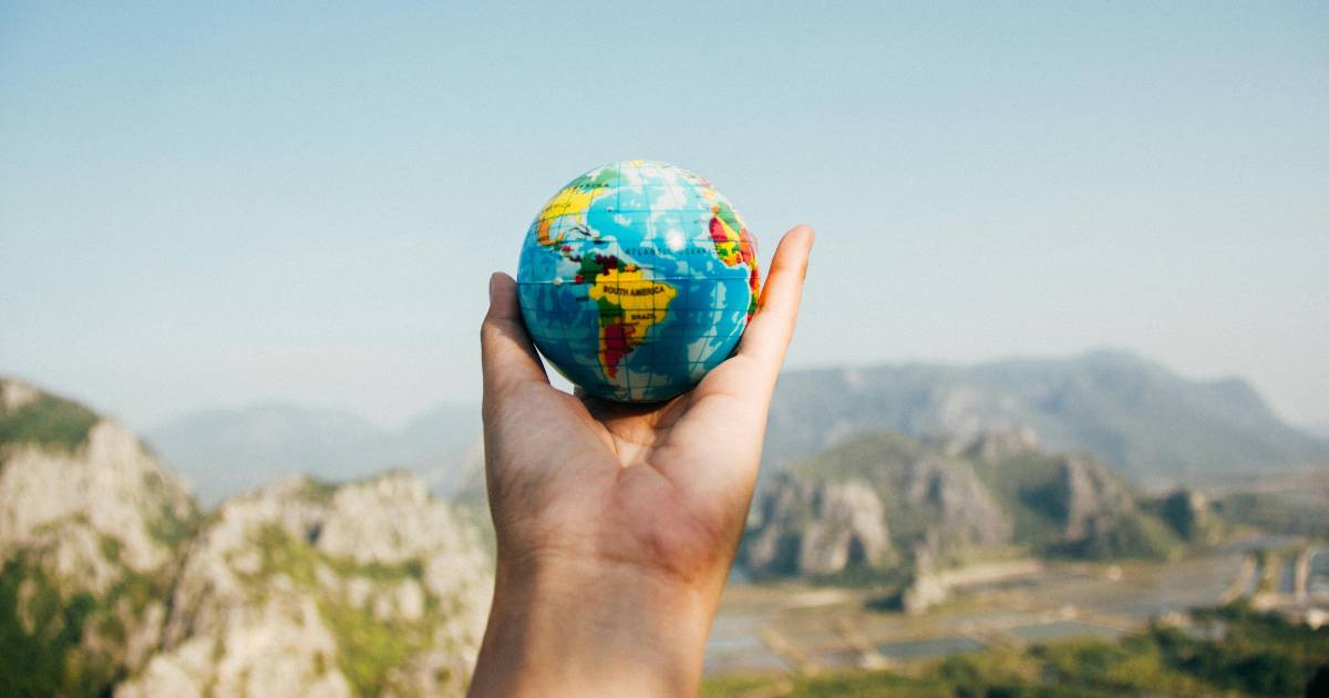 Person Holding World Globe Facing Mountain.