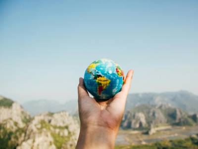 Person Holding World Globe Facing Mountain.