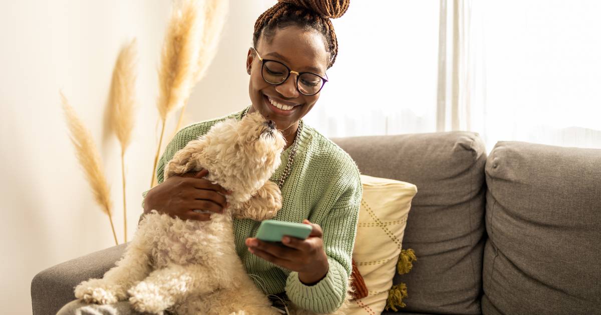 African American female student, at home with her dog, using a mobile phone.