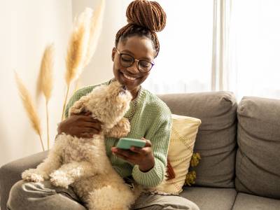 African American female student, at home with her dog, using a mobile phone.