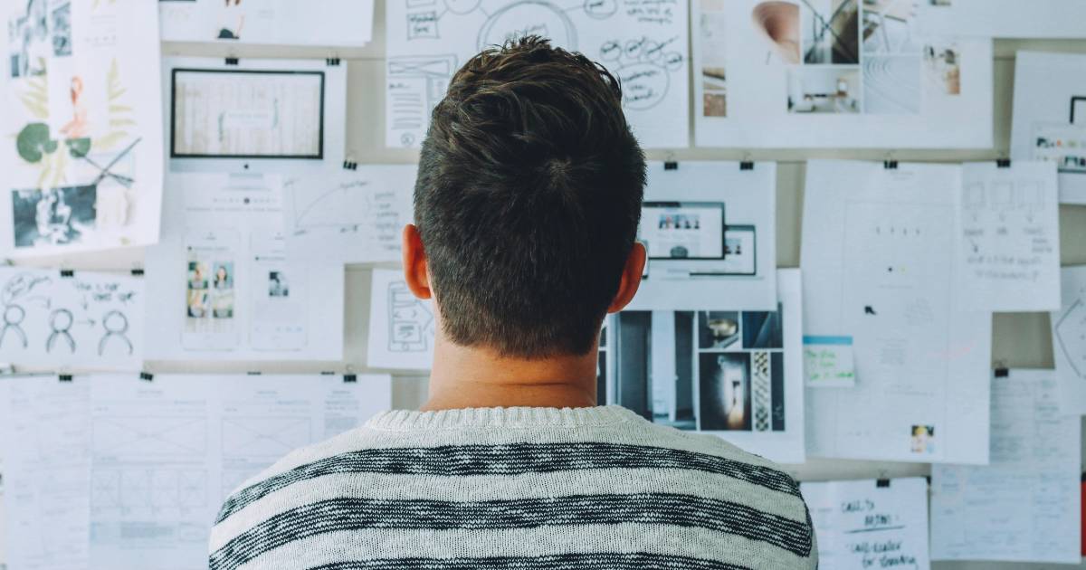 Man Wearing Black and White Stripe Shirt Looking at White Printer Papers on the Wall.