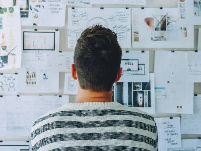 Man Wearing Black and White Stripe Shirt Looking at White Printer Papers on the Wall.