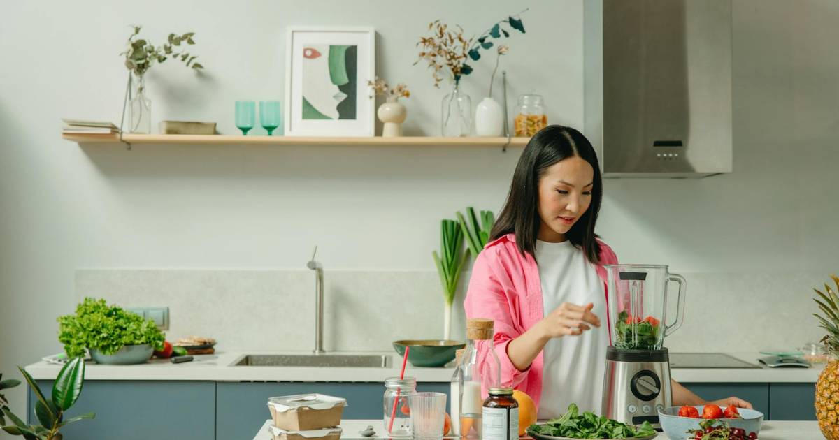 Woman at home preparing a juicer with fruits and greens.