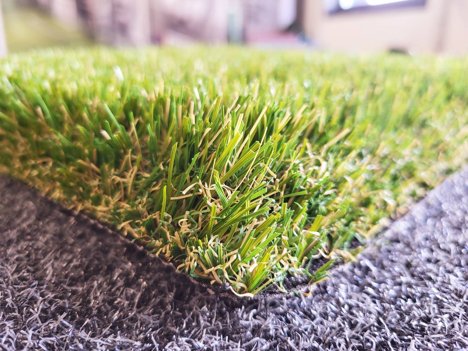 Gros plan sur un morceau de gazon artificiel vert avec une base noire visible.