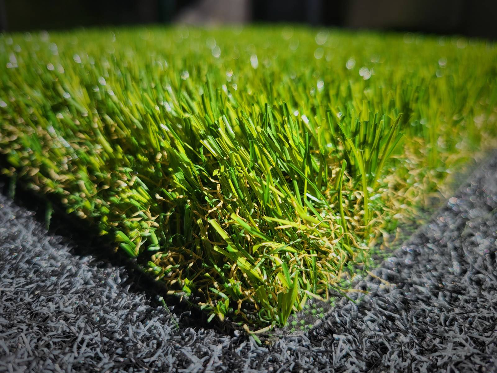 Gros plan sur une section de gazon synthétique vert vif posée sur un fond gris.