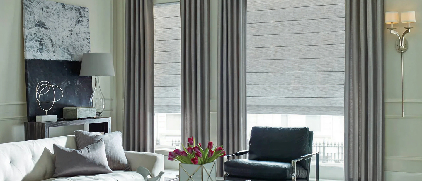Minimalist office with wooden desk, black chair, table lamp, flowers, and large windows with blinds.