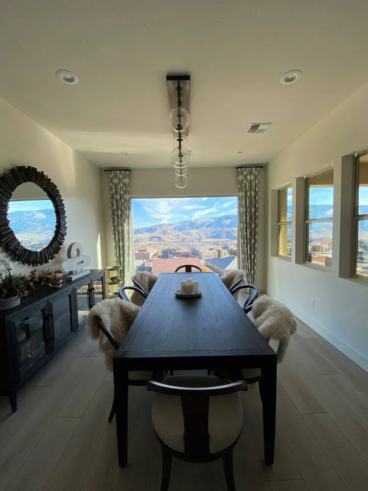 Dining room with black table, six chairs with fur covers, city and mountain view through large window.